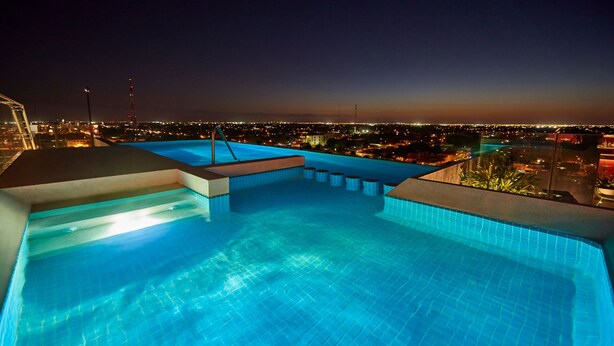 A rooftop infinity pool with a city view at night. - City Express Plus by Marriott Mérida (Mérida)