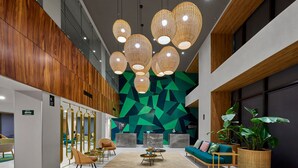 A modern lobby with a geometric wall design, wooden paneling, and a seating area with a sofa and chairs. - City Express Plus by Marriott Mérida (Mérida)