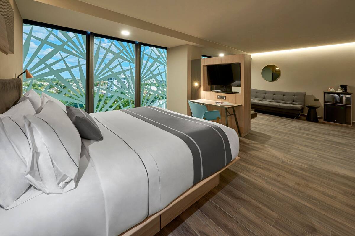 A modern hotel room with a large bed, a desk, a sofa, and a TV.