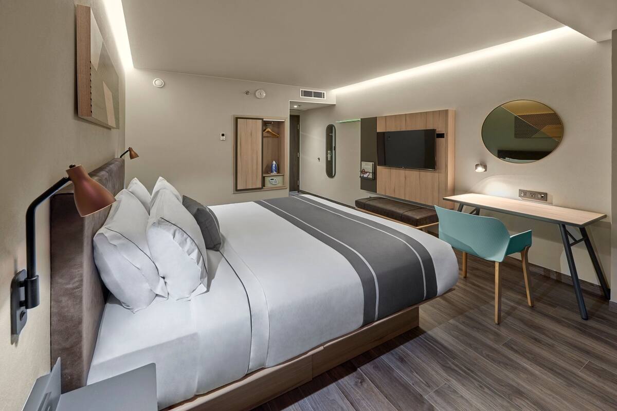 A modern hotel room with a bed, desk, chair, and a TV.
