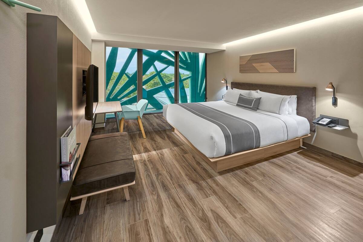 A modern hotel room with a large bed, a desk, a chair, and a TV.