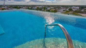 Ein klares, blaues Schwimmbecken mit Metallhandlauf, umgeben von einer Stadtlandschaft mit Gebäuden und Grünflächen.