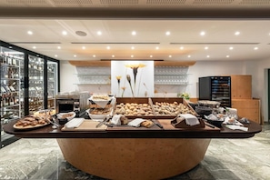 A buffet setup with various food items, a coffee machine, and a refrigerator.