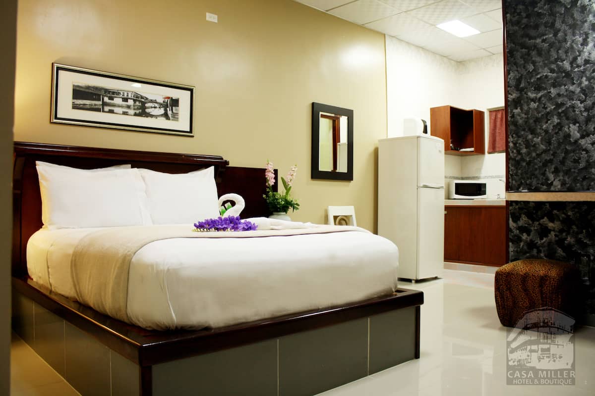 A hotel room with a bed, a small kitchenette, a mirror, and a framed picture on the wall.
