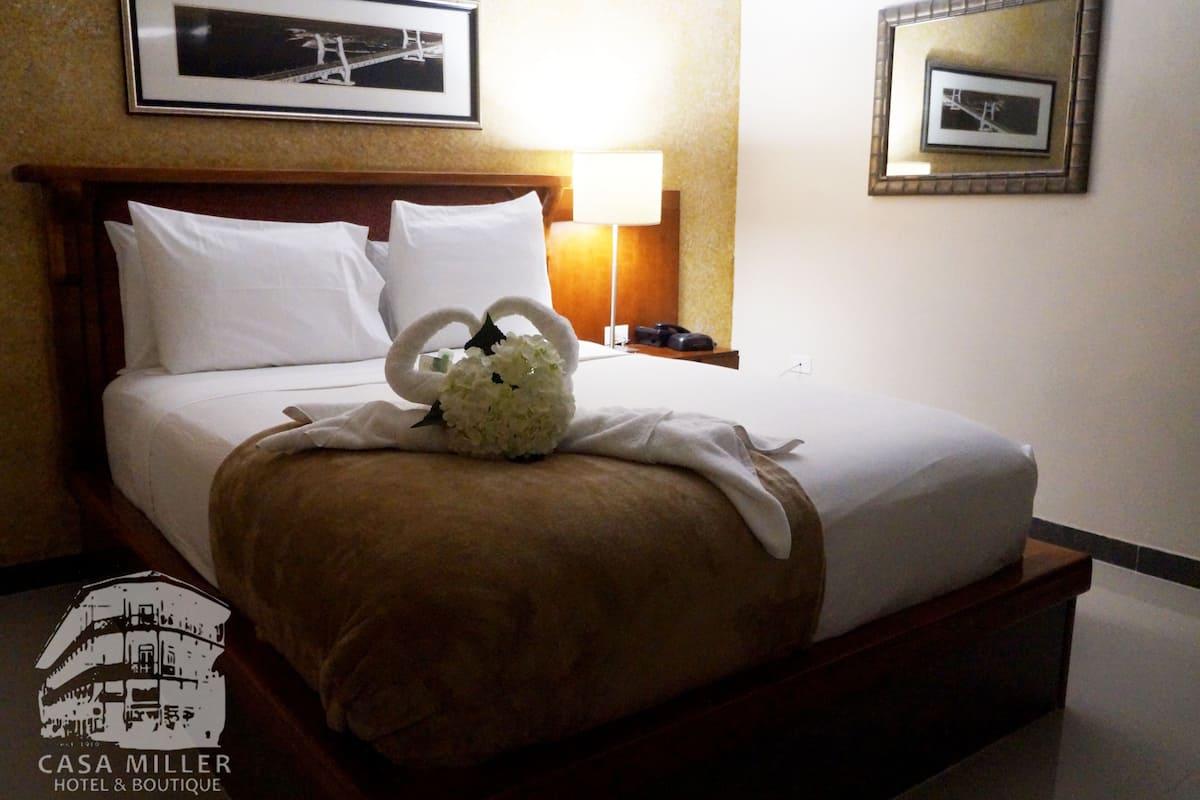 A neatly made bed with white linens, a brown throw blanket, and a decorative floral arrangement on the bed.