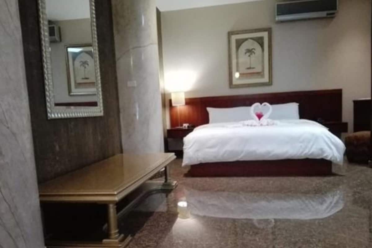 A hotel room with a bed, a nightstand, a mirror, and a framed picture on the wall.