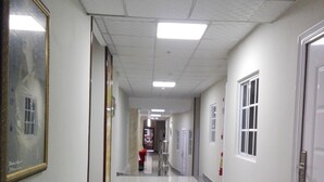 A long, narrow hallway with a tiled floor, white walls, and a ceiling with fluorescent lights. There are doors on both sides and a framed picture on the left wall. - Hotel Casa Miller (Panama City)