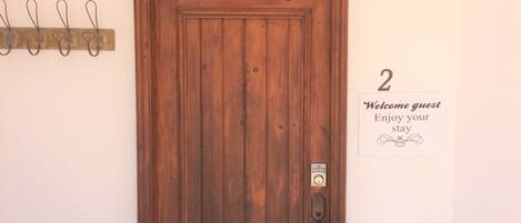 Una porta in legno con una serratura e un piccolo sistema di chiusura elettronica. Alla destra, una targa con il numero '2' e un messaggio di benvenuto.