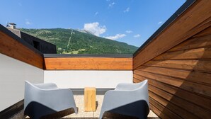 Eine Dachterrasse mit zwei grauen Stühlen und einem kleinen Holztisch, mit Blick auf eine gebirgige Landschaft.