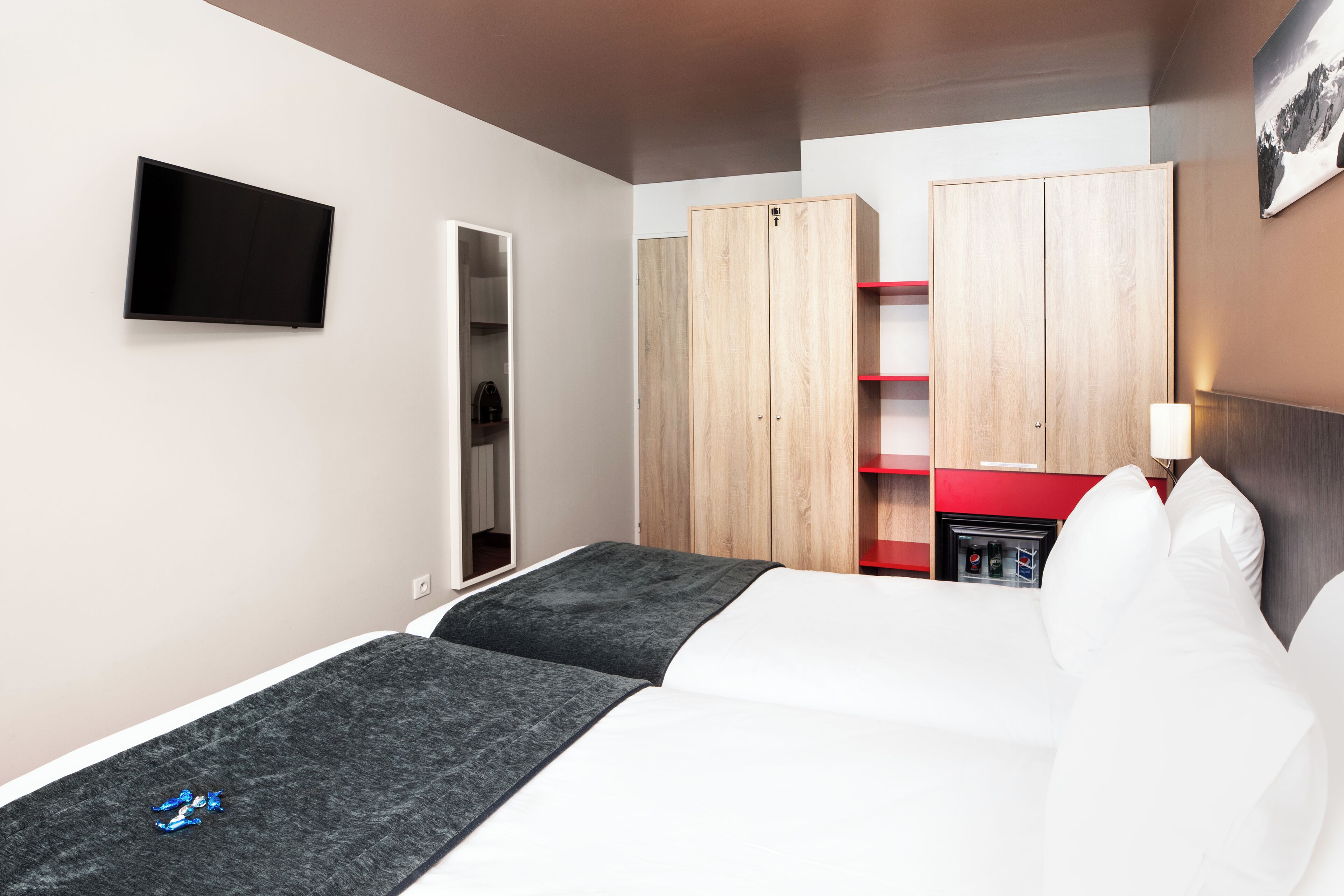 A hotel room with a bed, a TV, wardrobes, and a red-framed desk.