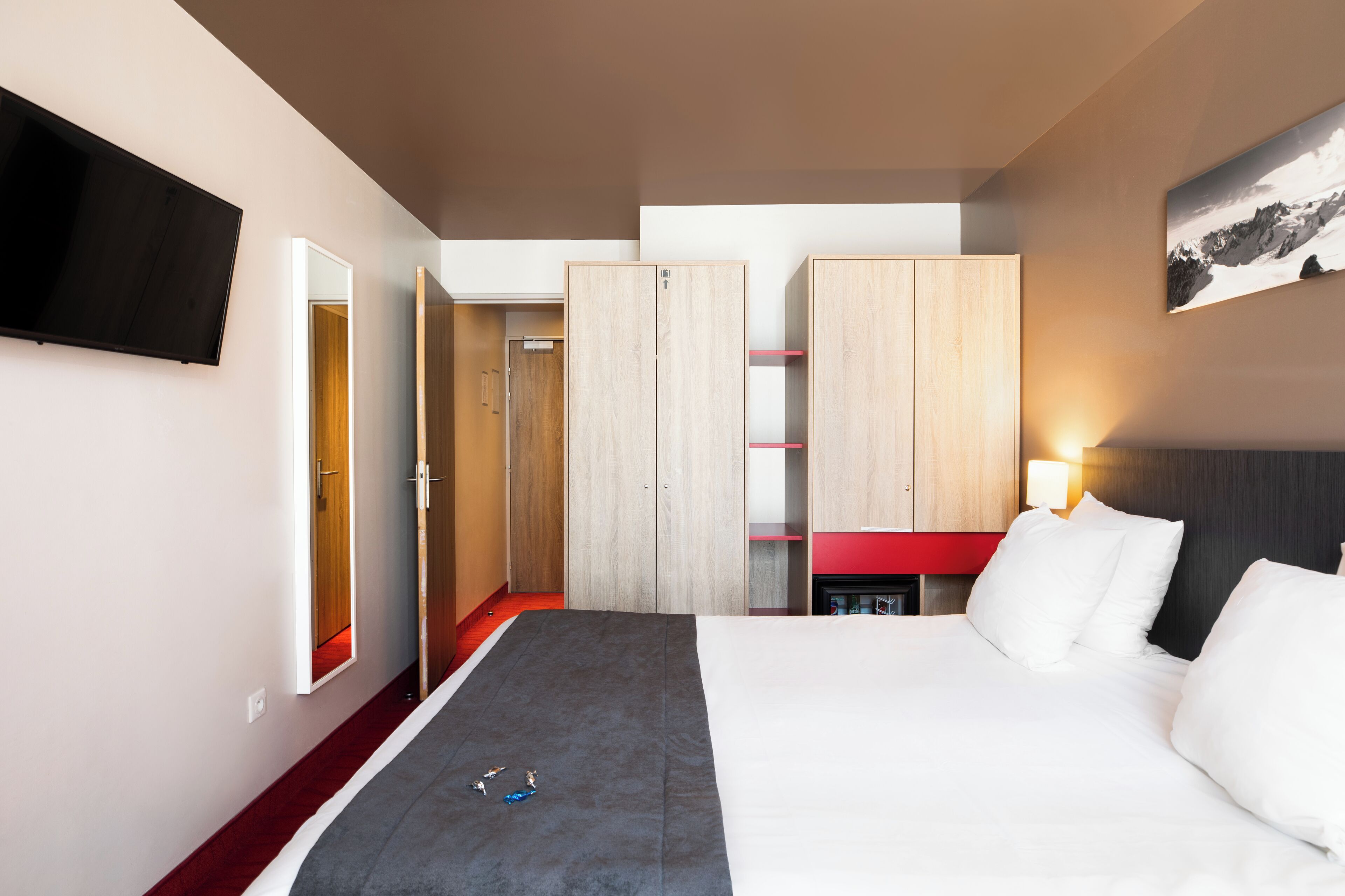 Une chambre d’hôtel avec un lit, un téléviseur fixé au mur, une armoire et un tableau accroché au mur.
