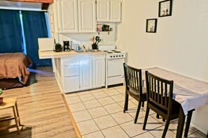 Uma cozinha compacta com armários brancos, um fogão e um espaço de refeições com duas cadeiras e uma mesa.
