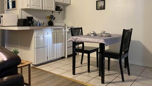 A compact kitchen with white cabinets, a microwave, and a coffee maker. There is a dining table with chairs and a small plant on the floor. - Arbor Inn Motel Oakridge (Oakridge)