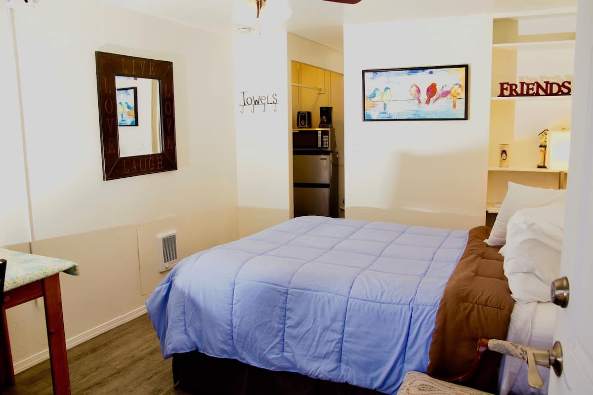Un dormitorio con una cama, una mesita de noche, un espejo, un marco de fotos y una pared con un cartel de 'Friends'.