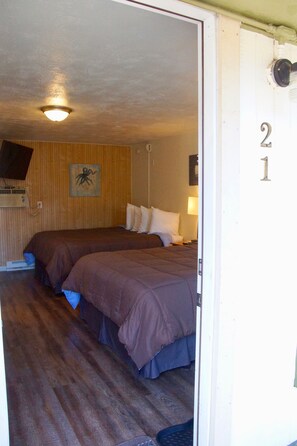 Quarto com duas camas, parede de madeira, luminária no teto e porta com o número 21.