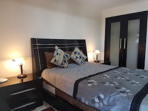 A neatly made bed with patterned bedding, two bedside lamps, a dark headboard, and a wardrobe with mirrored doors.