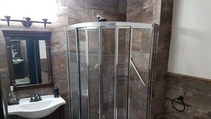 Une salle de bain avec une douche à parois de verre, un lavabo avec un distributeur de savon et des toilettes.