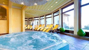Een wellnessruimte met een jacuzzi, ligbedden en grote ramen.