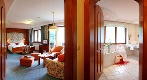 Une chambre d’hôtel comprenant un lit, un coin salon avec un canapé et des fauteuils, une petite table avec une lampe, et une salle de bain avec une baignoire et un lavabo.