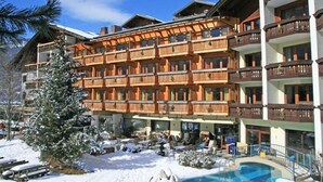 Een hotel met meerdere verdiepingen, balkons, een zwembad en een besneeuwde omgeving.