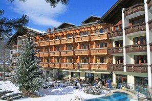 Un hôtel à plusieurs étages doté de balcons, d’un espace piscine et entouré d’un paysage enneigé.