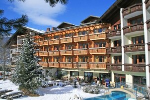 Un hotel de varios pisos con balcones, una zona de piscina y alrededores nevados.