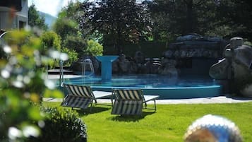 A swimming pool with lounge chairs, a water feature, and a rock formation.