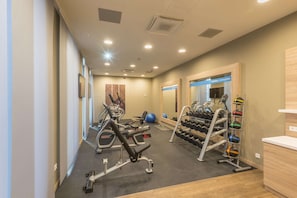 Un gimnasio con equipo de ejercicio, un estante de mancuernas y un espejo.