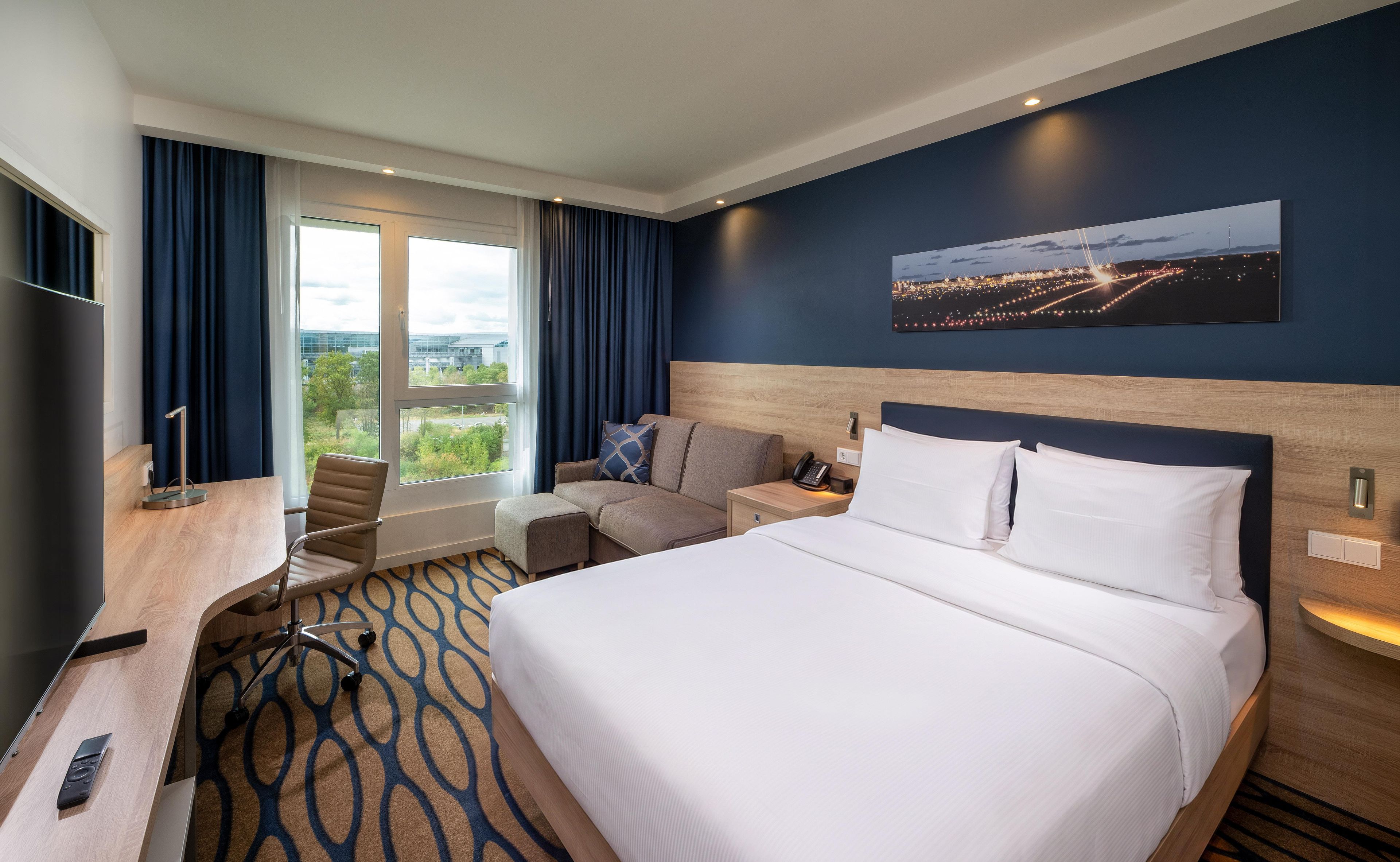 Een hotelkamer met een groot bed, een bureau, een stoel, een nachtkastje en uitzicht op de stad 's nachts.