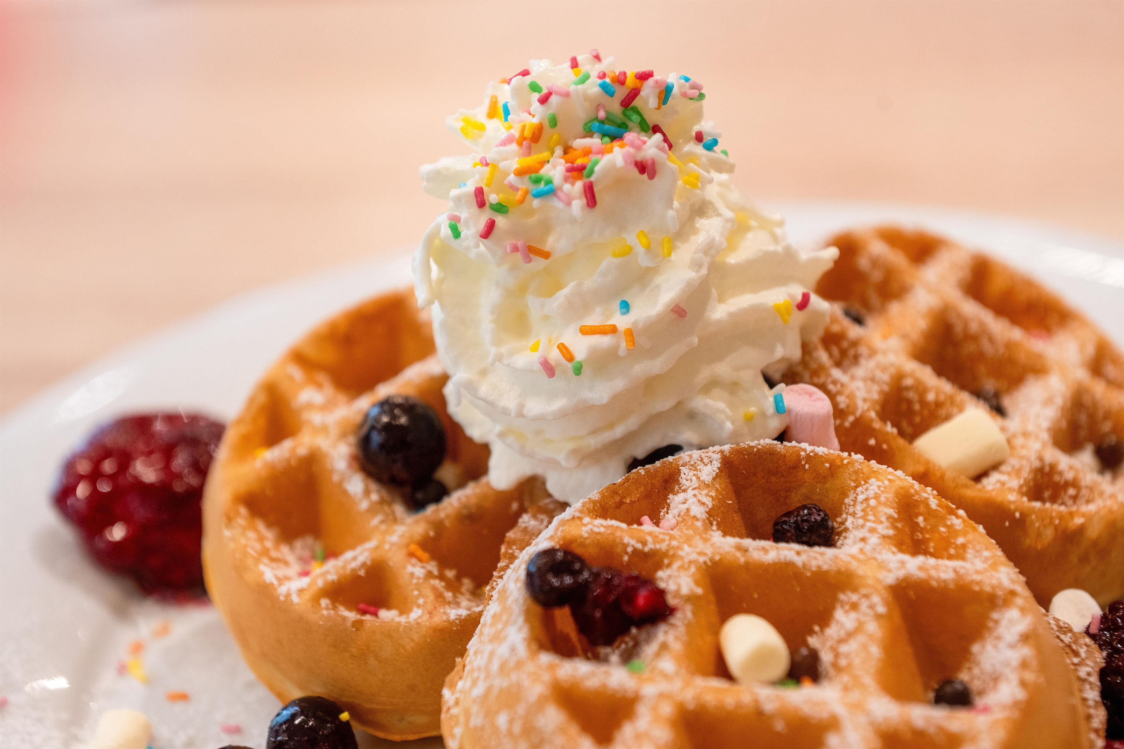 Ein Teller Waffeln mit Schlagsahne und bunten Streuseln, dazu Beeren und Schokoladenstückchen.