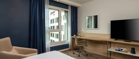 A hotel room with a bed, a desk, a chair, a television, and a window with curtains.