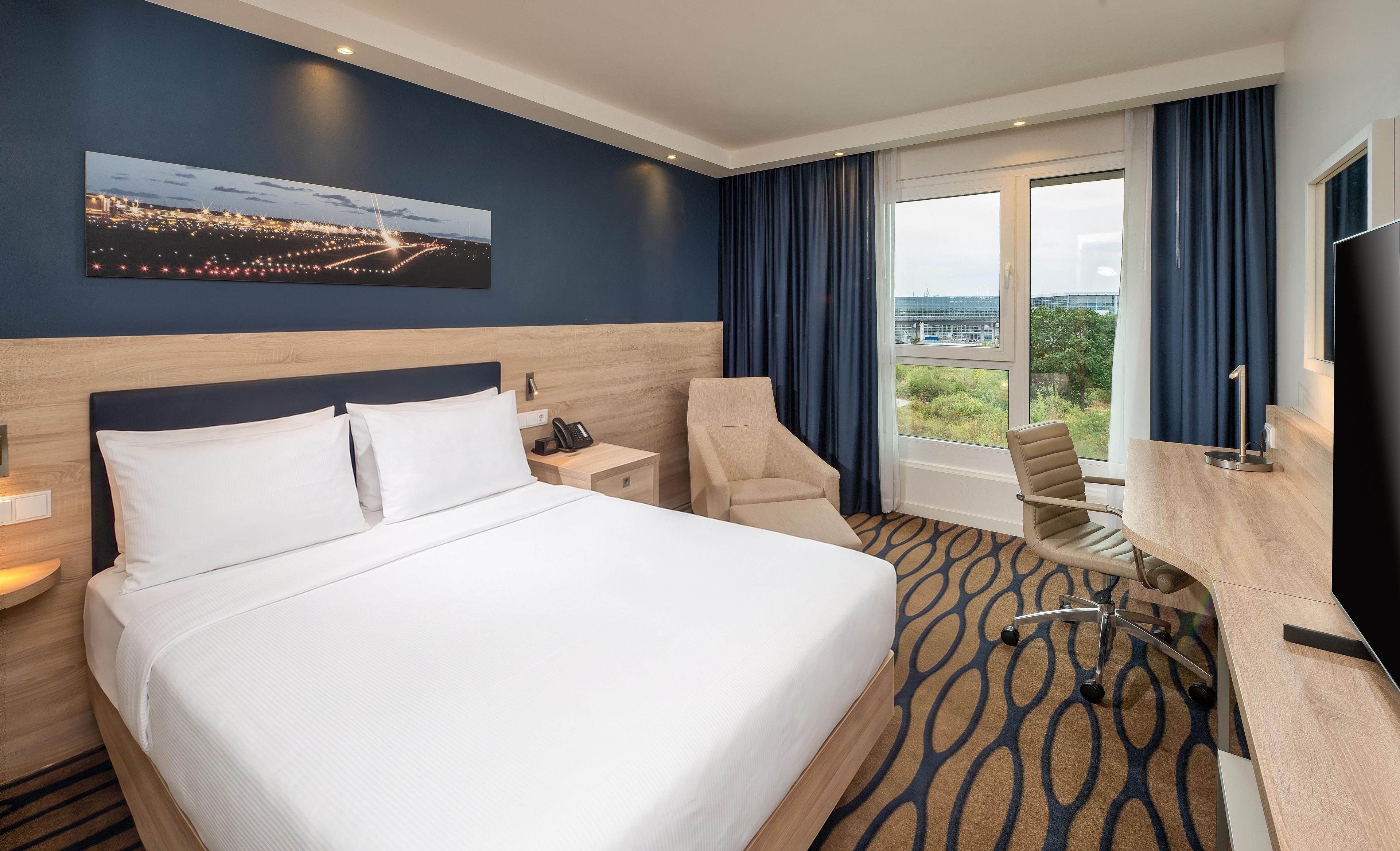 Una habitación de hotel con una cama grande, un escritorio, una silla, un televisor y una ventana con cortinas.