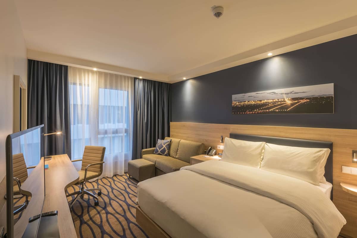 Ein Hotelzimmer mit einem großen Bett, einem Schreibtisch mit Stuhl, einem Fernseher und einem Stadtbild an der Wand.