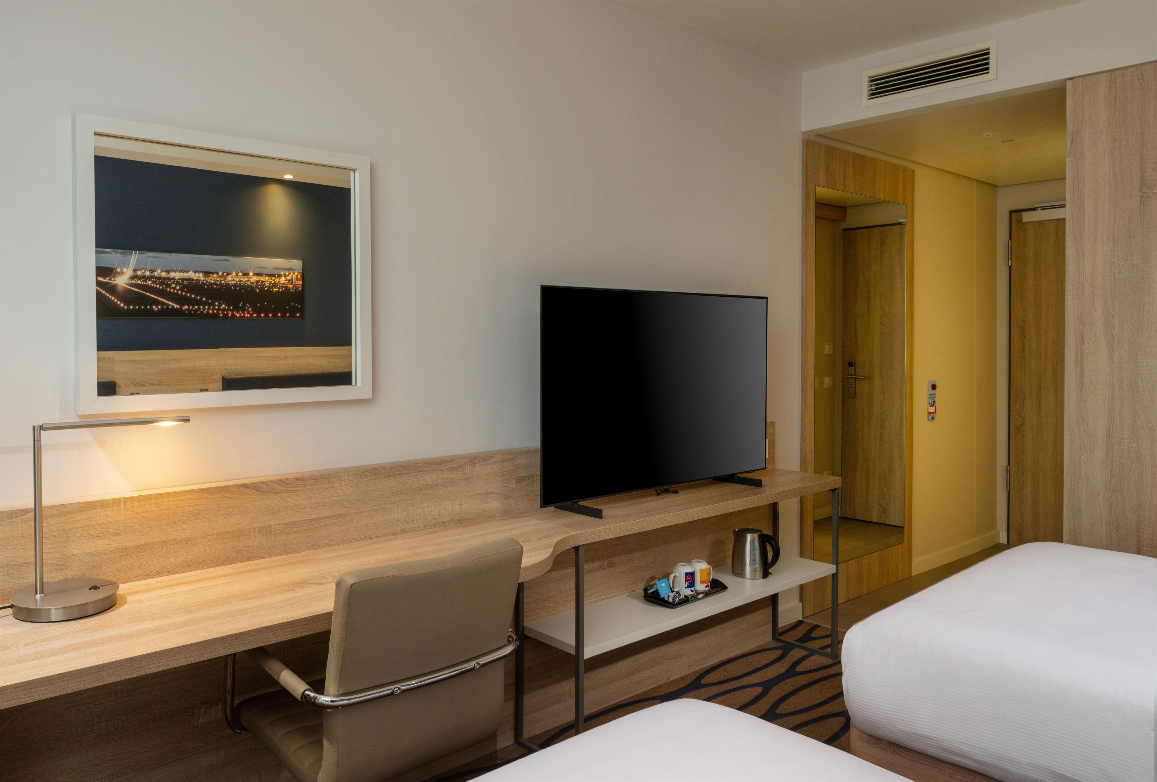 Habitación de hotel con una televisión de pantalla plana, un escritorio con una silla, una cama y un cuadro en la pared.