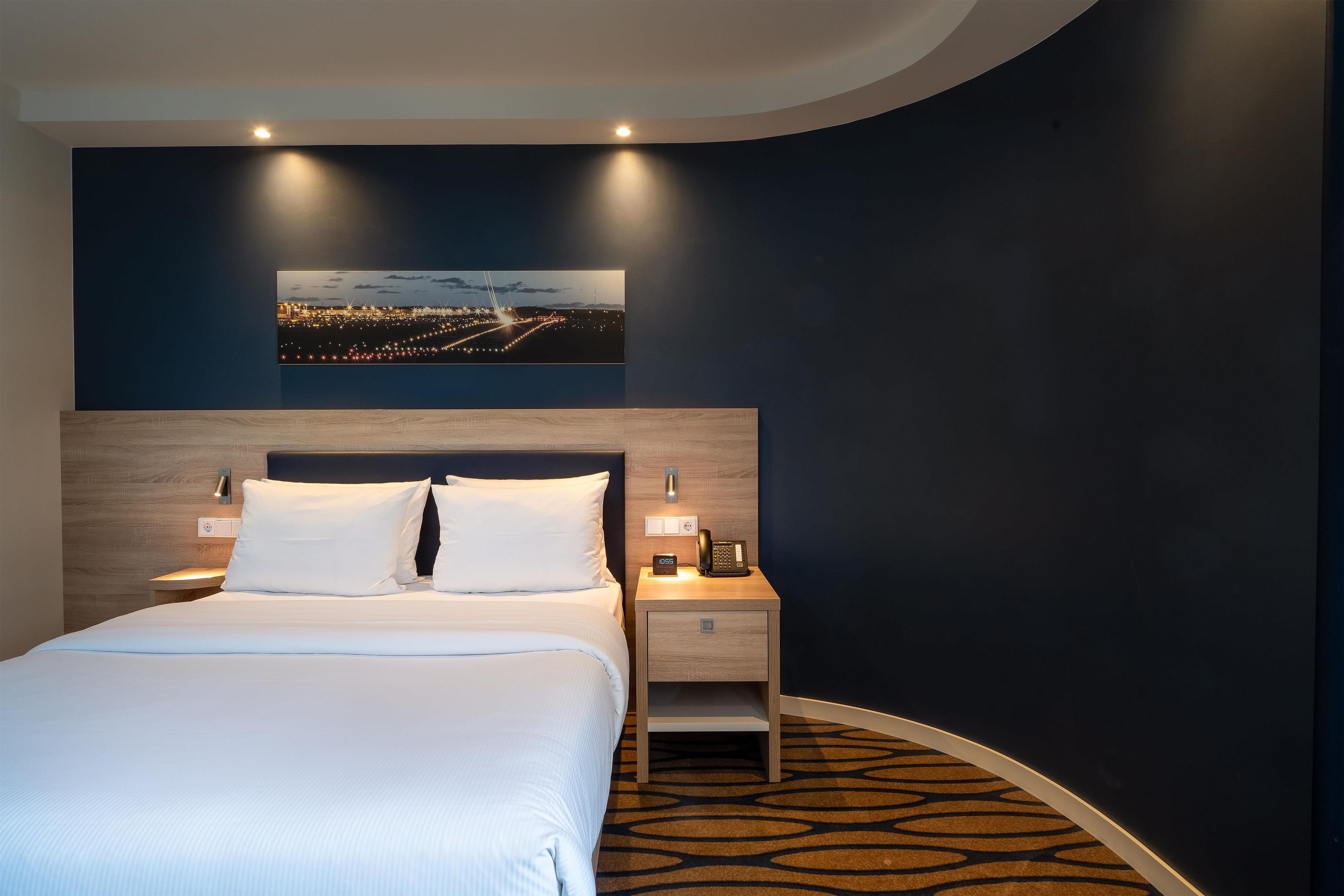 Habitación de hotel con cama, mesitas de noche, un teléfono y un cuadro colgado en la pared.