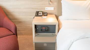 Habitación de hotel con pared de madera, mesita de noche con teléfono, caja fuerte y cama con ropa blanca.