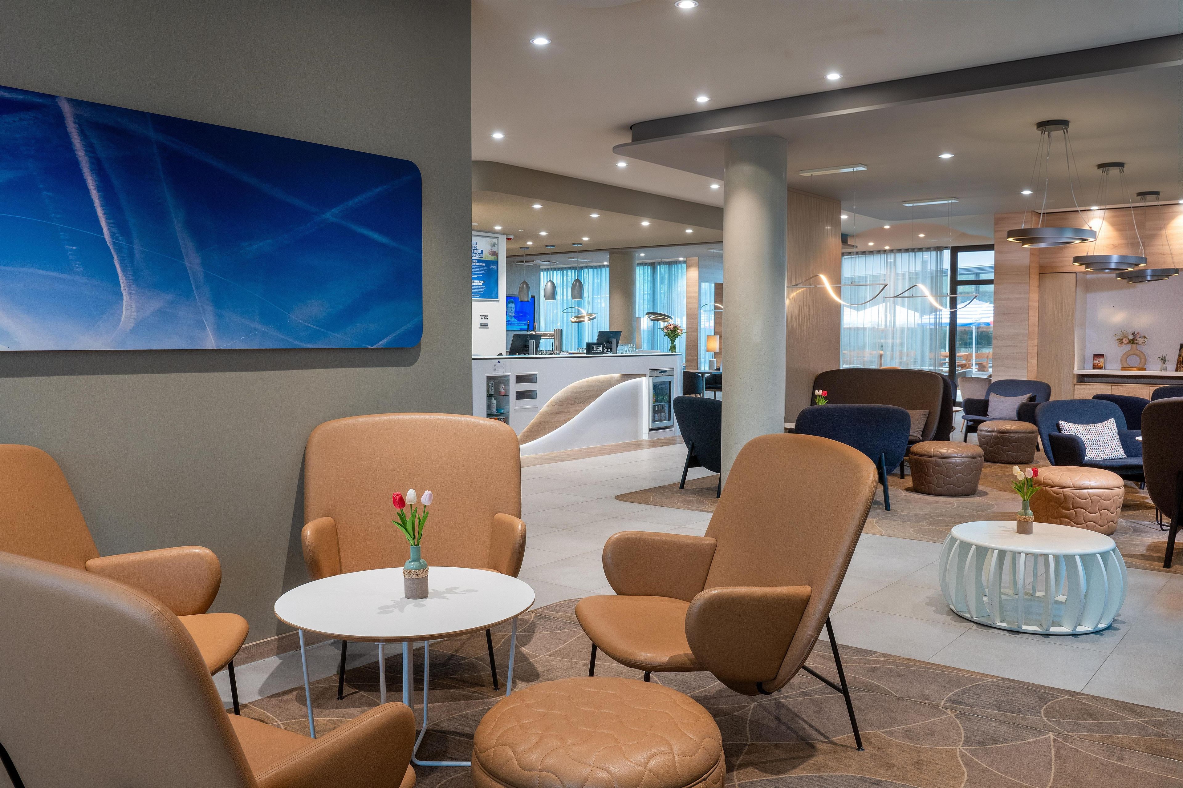 A modern lounge area with leather chairs, a round table, and a blue abstract painting on the wall.