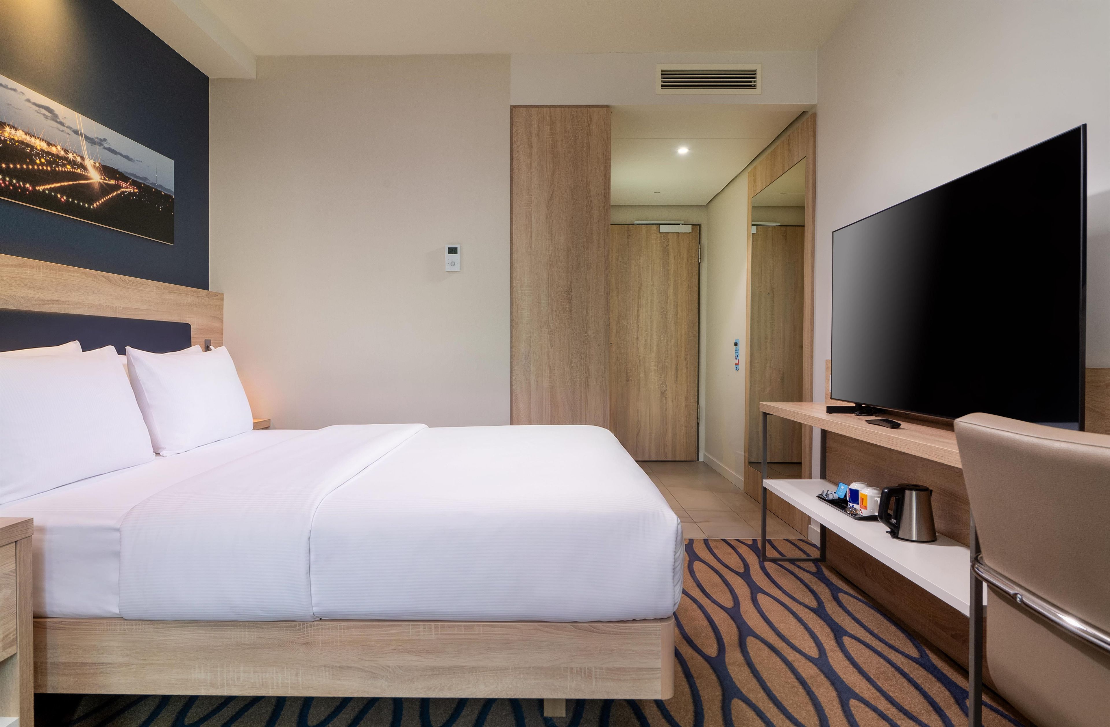 A hotel room with a bed, a television, a desk, and a bathroom door.