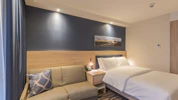 Una habitación de hotel con una cama, un sofá, una mesita de noche con lámpara y un cuadro colgado en la pared.