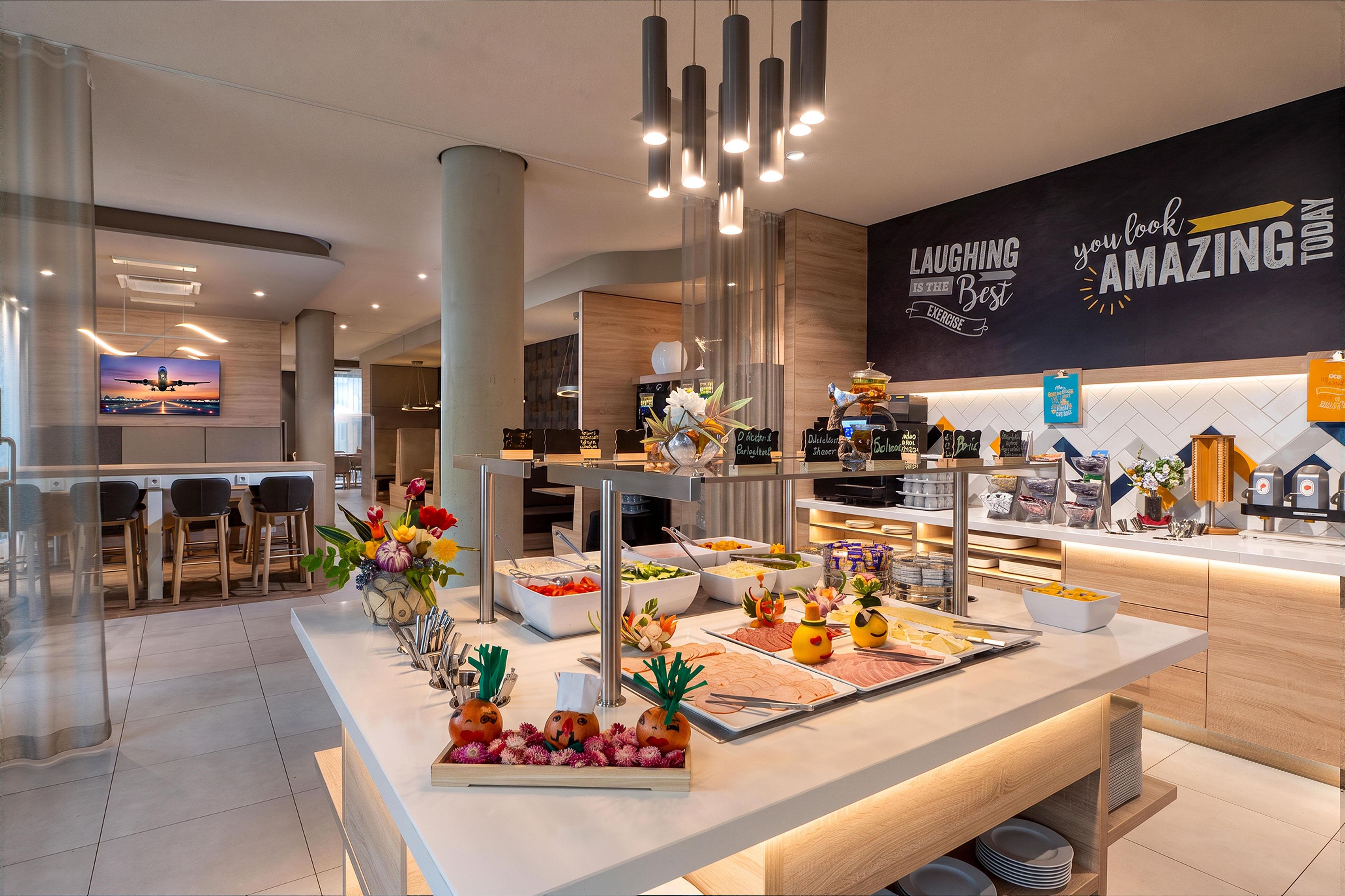 Un moderno vestíbulo de hotel con una zona de bufé que ofrece diversas opciones de comida y una pared decorativa con citas inspiradoras.