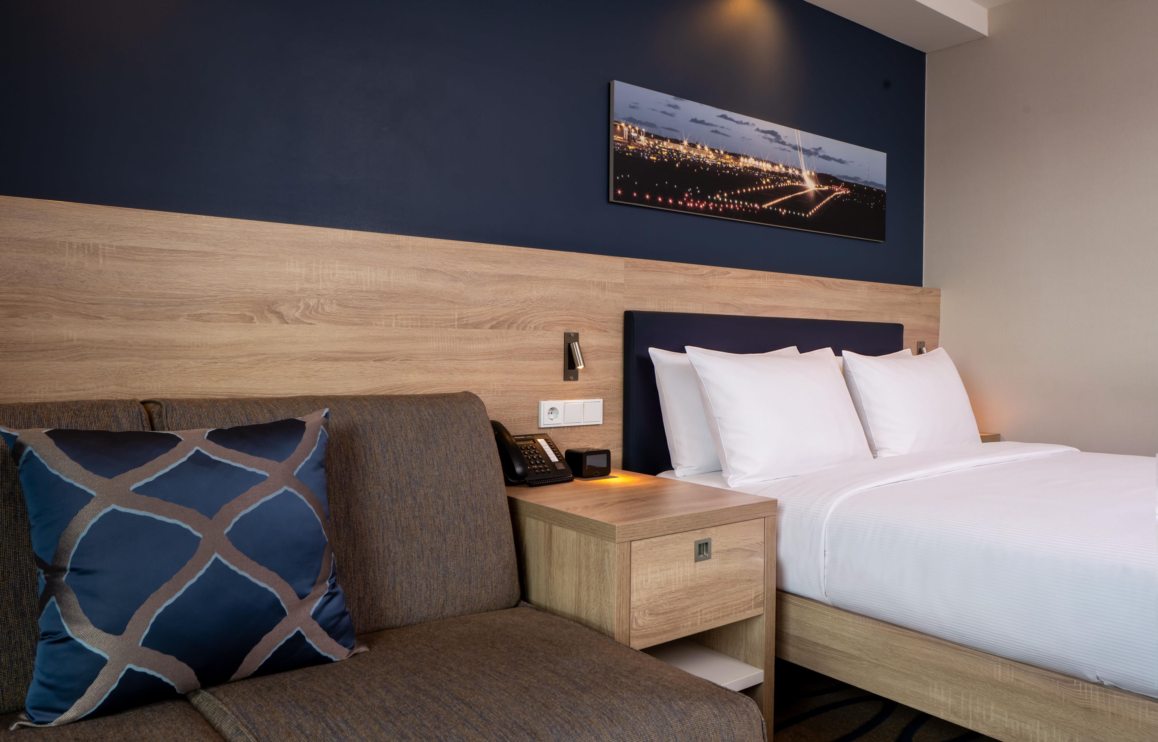 A hotel room with a bed, a nightstand, a telephone, and a wall-mounted picture.