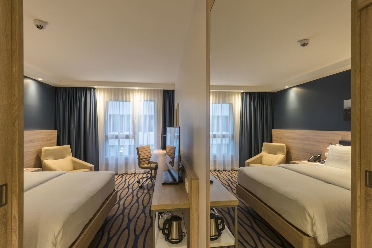Habitación de hotel con dos camas, un escritorio, una silla, una cafetera y un teléfono.