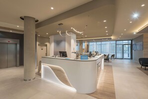 Una moderna zona de recepción de hotel con un mostrador central, un pilar grande y vistas al vestíbulo.