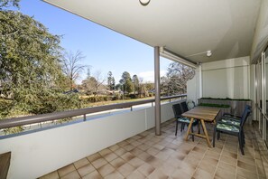 Un balcón con suelo de baldosas, una mesa con sillas y vistas a árboles y edificios.