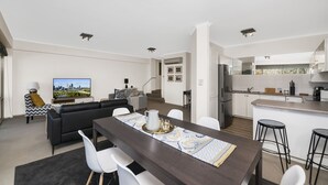 En modern lägenhet med matplats, vardagsrum, kök och en tv-skärm som visar en stadsbild.