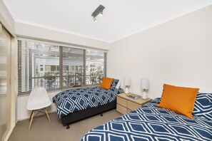 Un dormitorio con dos camas, una silla, una mesita de noche y una ventana con persianas.