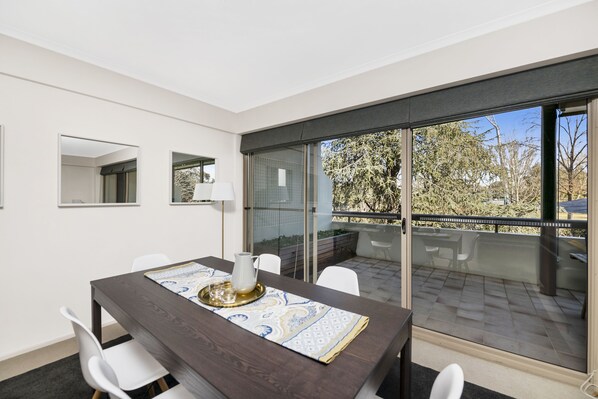 Un espace repas moderne avec une table en bois foncé, des chaises blanches et une cloison en verre.