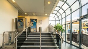 A staircase with metal railings leading to an upper floor, a glass wall with a view of the street, and a poster on the wall. - Ibis Budget London Whitechapel - Brick Lane (London)