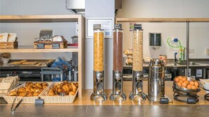 A breakfast buffet with labeled food containers, a clock, and a coffee machine. - Ibis Budget London Whitechapel - Brick Lane (London)