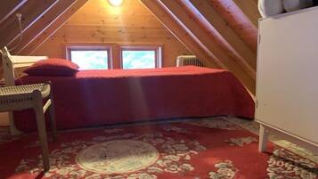 A cozy attic bedroom with a red bedspread, a wooden chair, and a patterned carpet.
